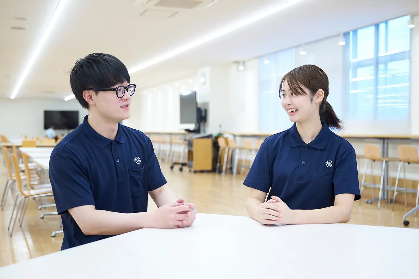 UNION TOOLのロゴ付きポロシャツを着た2人の社員がテーブルで会話している様子